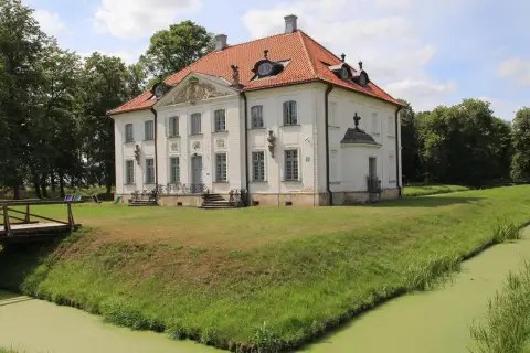 PaÅac w Choroszczy otoczony fosÄ i zieleniÄ. Drewniany mostek prowadzi do rezydencji.